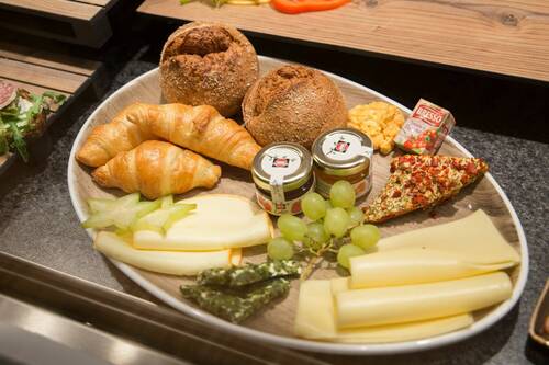Frühstücksteller mit Käseauswahl, Croissants, Vollkornbrötchen, Trauben, Frischkäse, Marmelade und Butter.