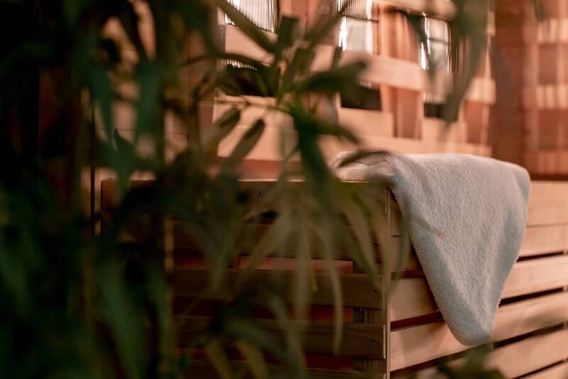 Close-up of a wellness area with wooden sauna bench, towel and green plant in the foreground.