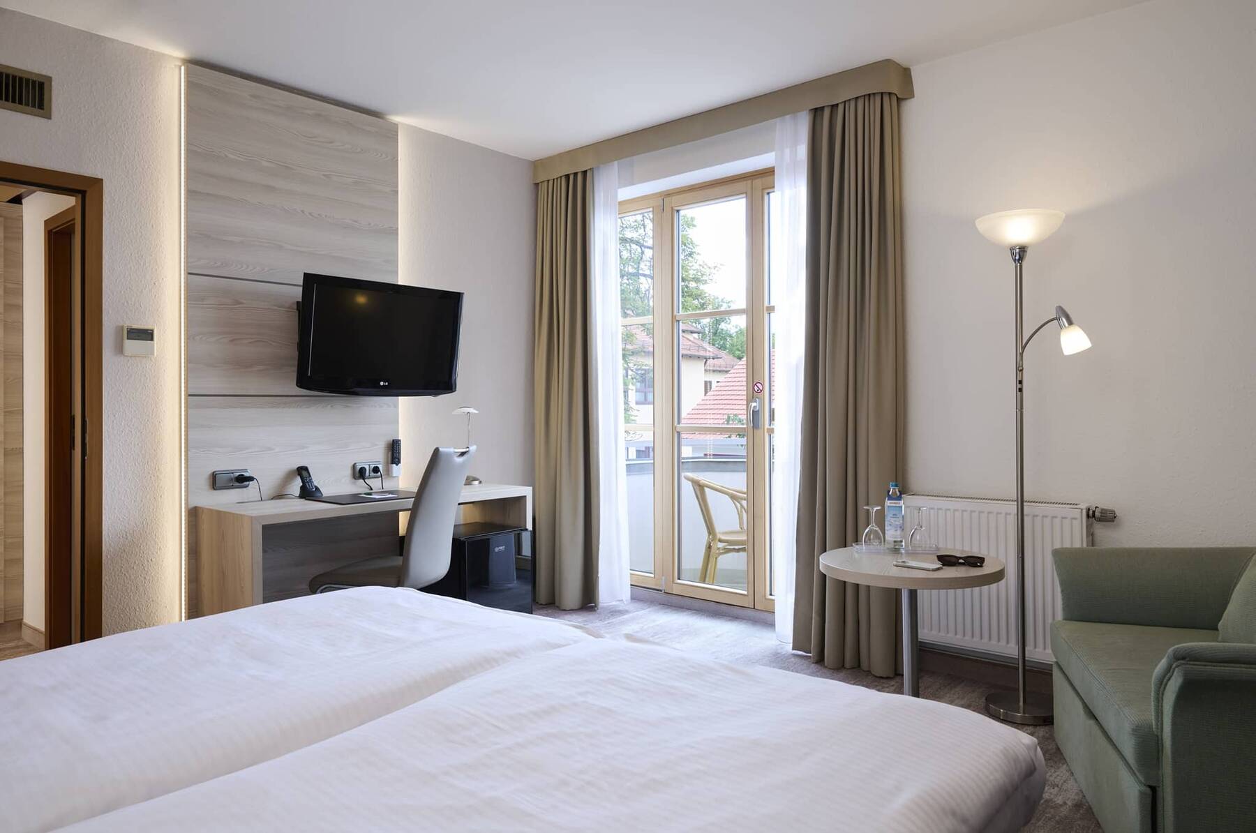 Helles Doppelzimmer mit Balkon im Hotel Kastanienhof Erding mit komfortablem Doppelbett, Sitzecke und praktischem Arbeitsplatz.