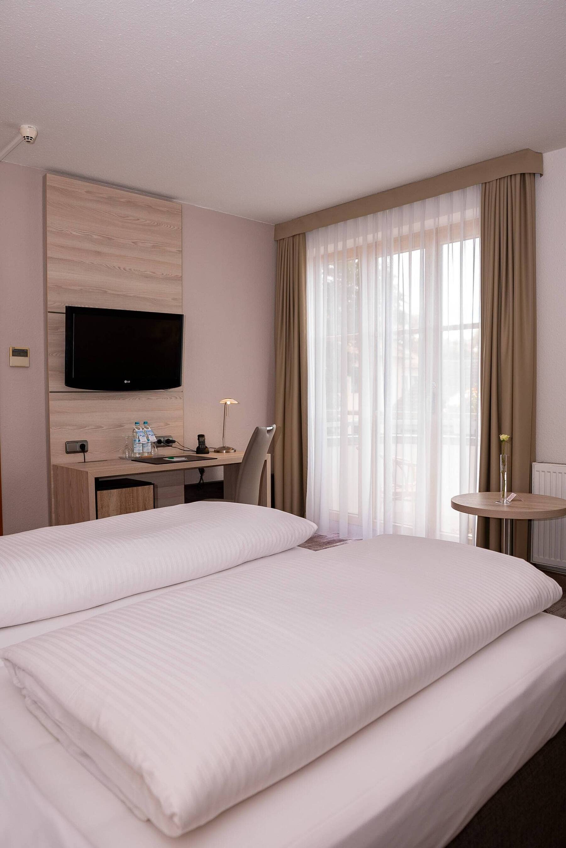 Doppelzimmer der Familiensuite im Hotel Kastanienhof Erding mit Balkonzugang, Schreibtisch, Flachbild-TV und gemütlichem Doppelbett.