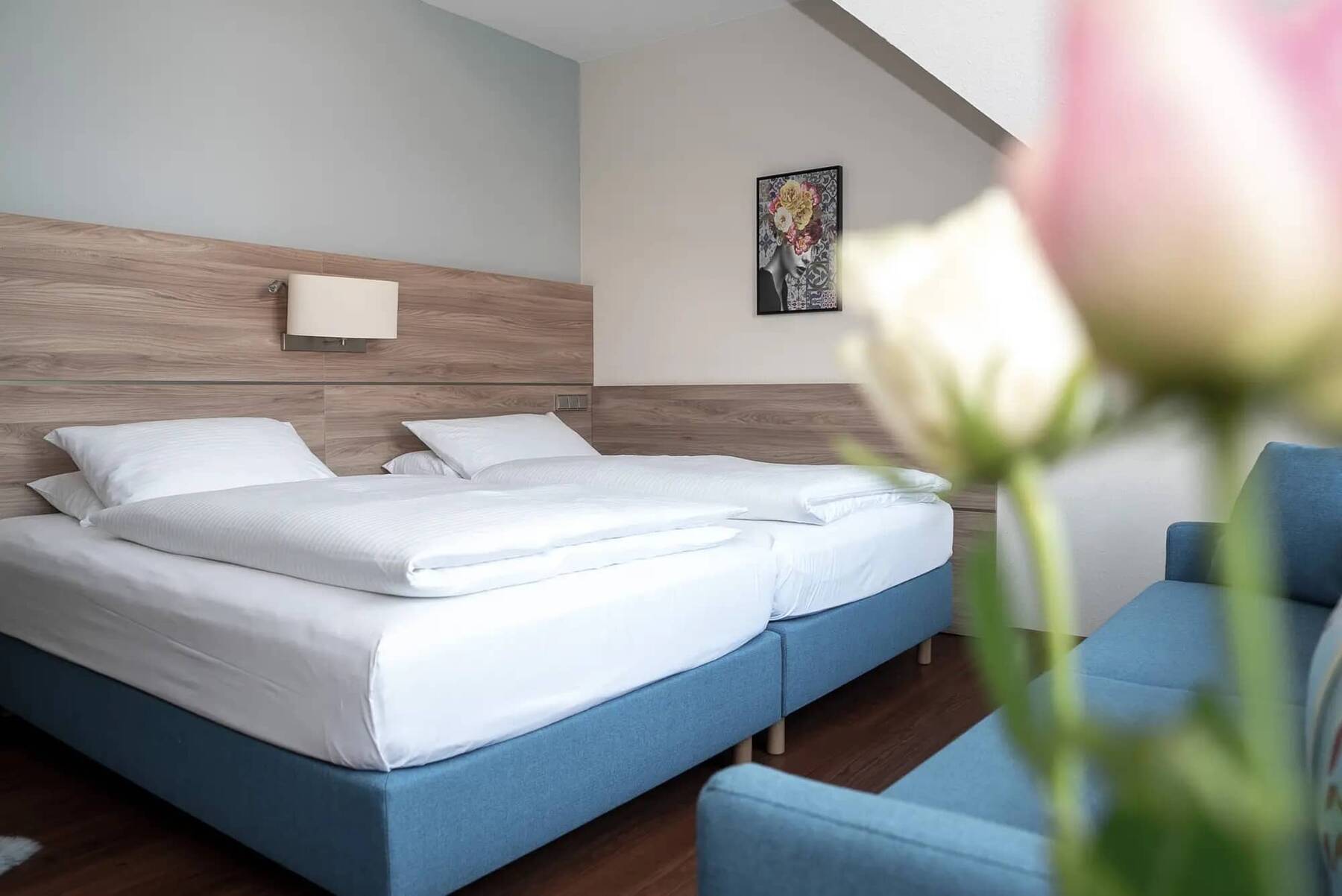 Modernes Doppelzimmer mit großem Doppelbett in pastell-blauem Farbton, Holzpaneele an der Wand und einem Zweisitzer-Sofa vor dem Bett, ebenfalls in pastell-blau.