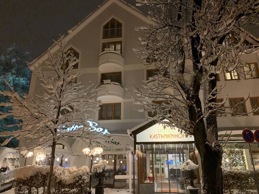 Das Hotel Kastanienhof im Winter: Der Eingang ist beleuchtet, davor stehen zwei schneebedeckte Bäume.