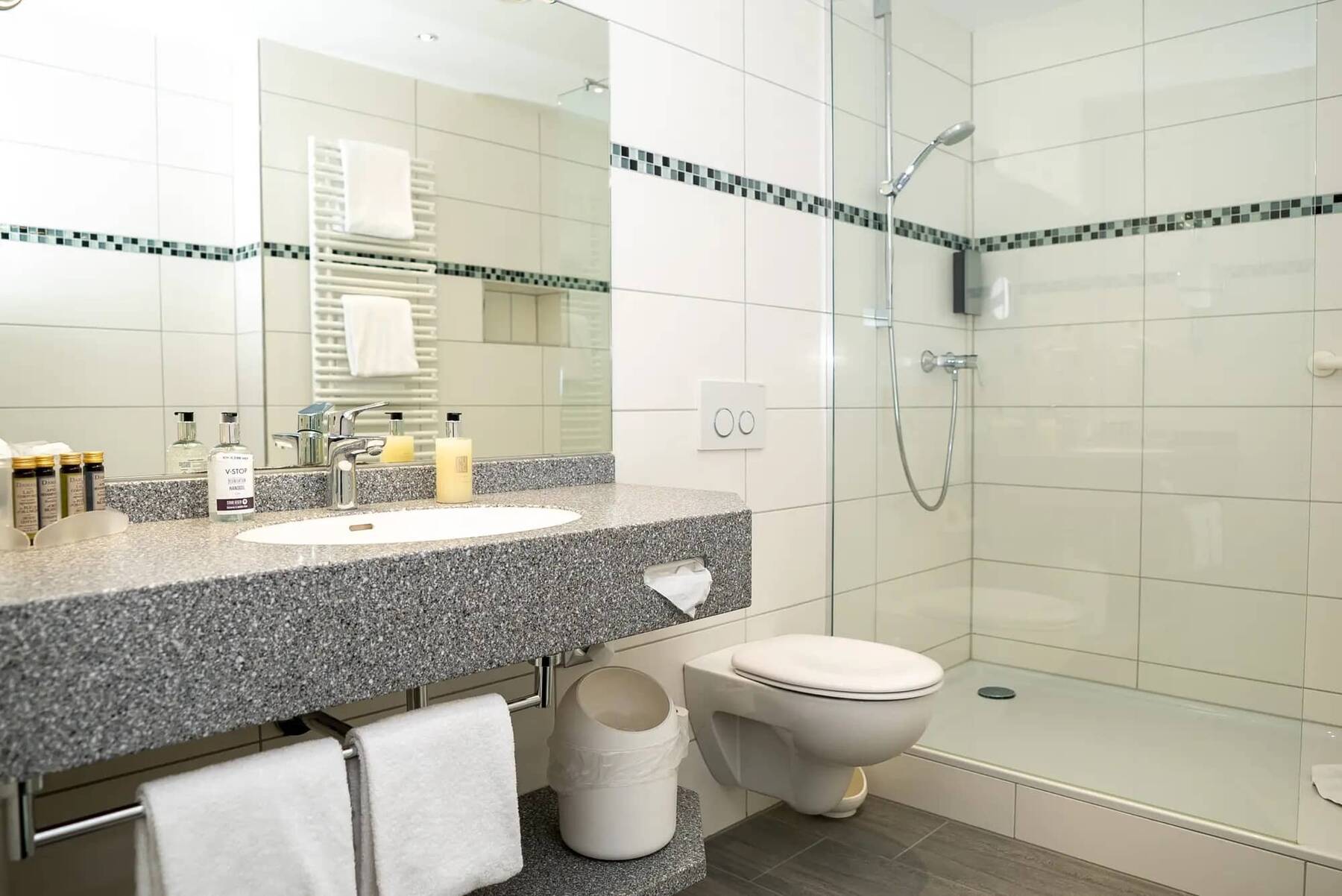 Modernes Badezimmer im Hotel Kastanienhof Erding mit großer Dusche, Waschtisch aus Granit, Handtuchhalter und hochwertigen Pflegeprodukten.