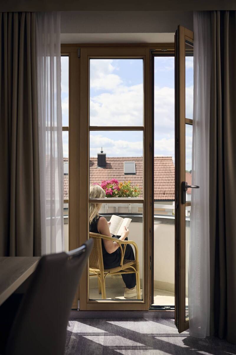 Sonniger Balkon eines Doppelzimmers im Hotel Kastanienhof Erding mit Sitzgelegenheit und Blick über die Dächer von Erding.