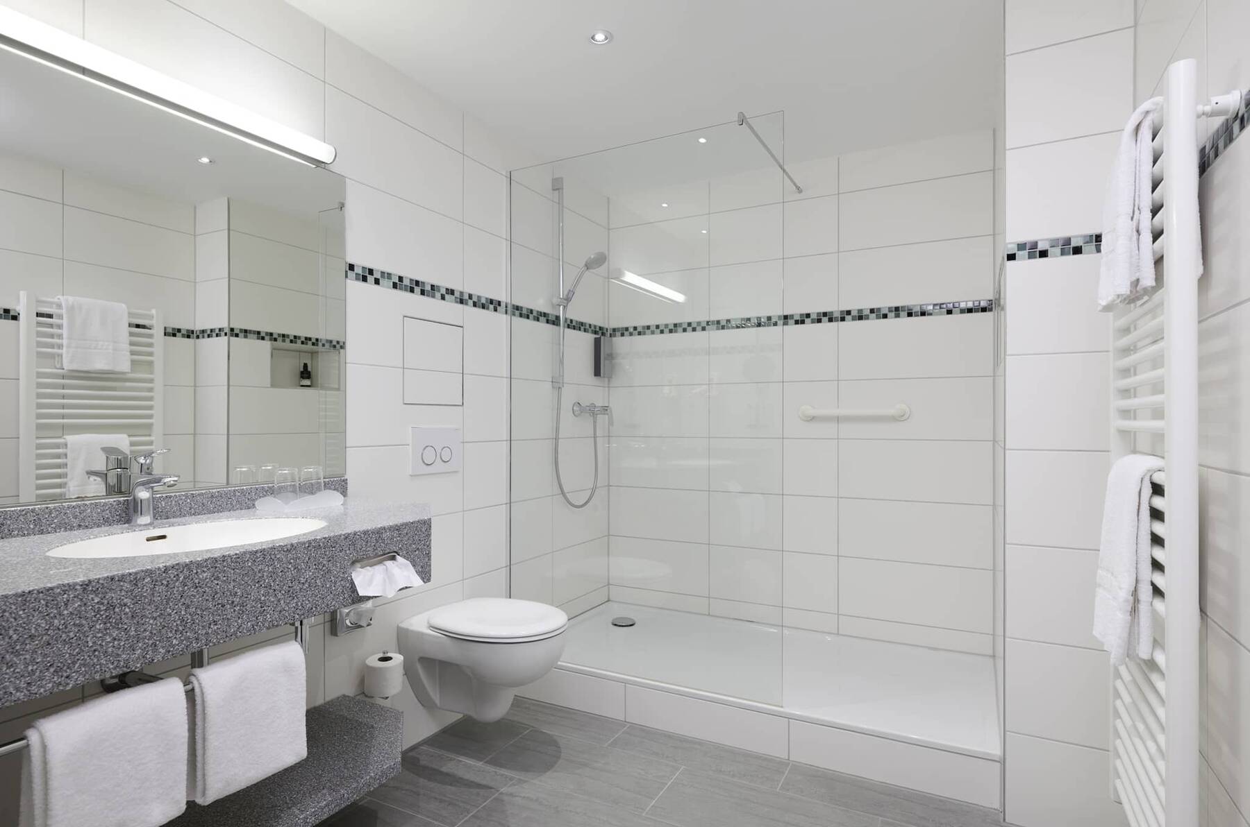 Helles Badezimmer des Executive Doppelzimmers im Hotel Kastanienhof Erding mit großer Dusche, Waschbecken und Handtuchheizkörper.