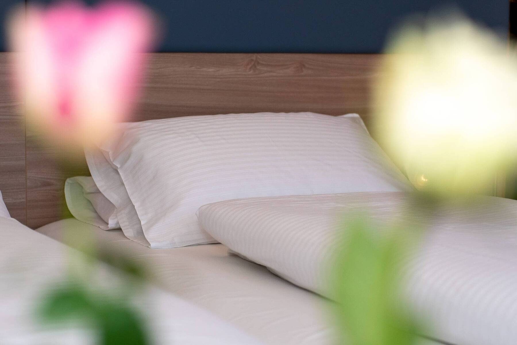 Gemütliches Hotelzimmer im Kastanienhof Erding mit frischer Bettwäsche und weichen Kissen, im Vordergrund unscharfe Tulpen als wohnlicher Akzent.