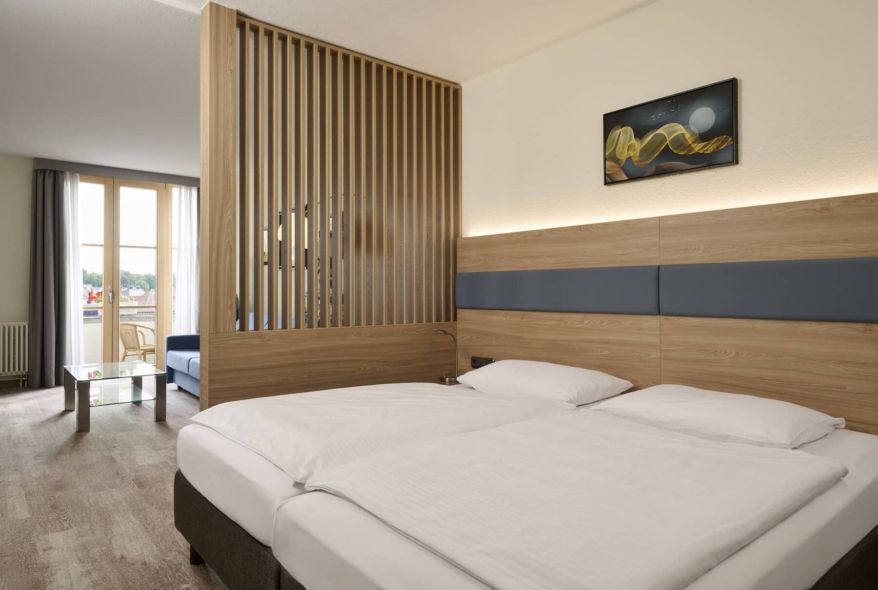 Heller Schlafbereich des Executive Doppelzimmers im Hotel Kastanienhof Erding mit komfortablem Doppelbett, Wohnbereich und Balkon.