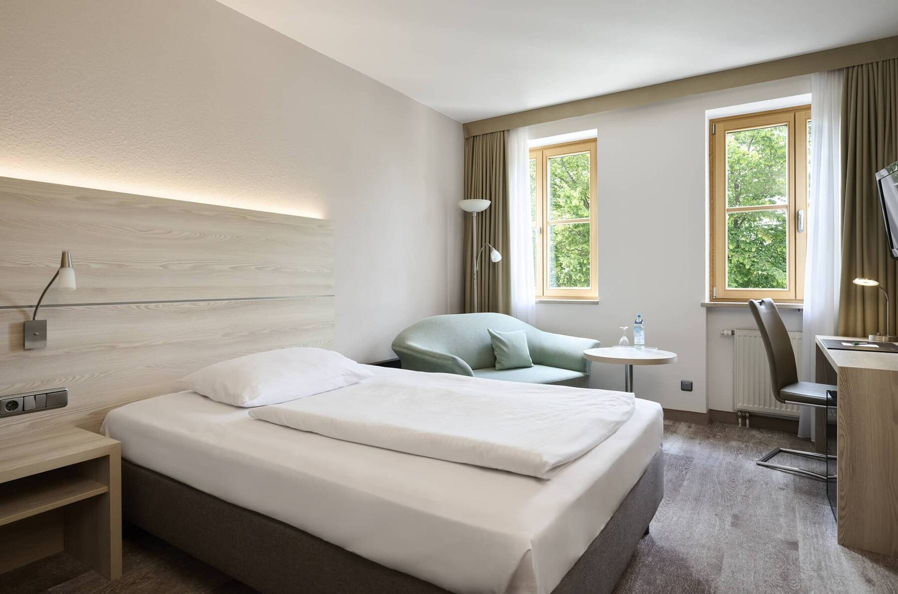 Helles Einzelzimmer im Hotel Kastanienhof Erding mit komfortablem Bett, gemütlicher Sitzecke und praktischem Arbeitsplatz.