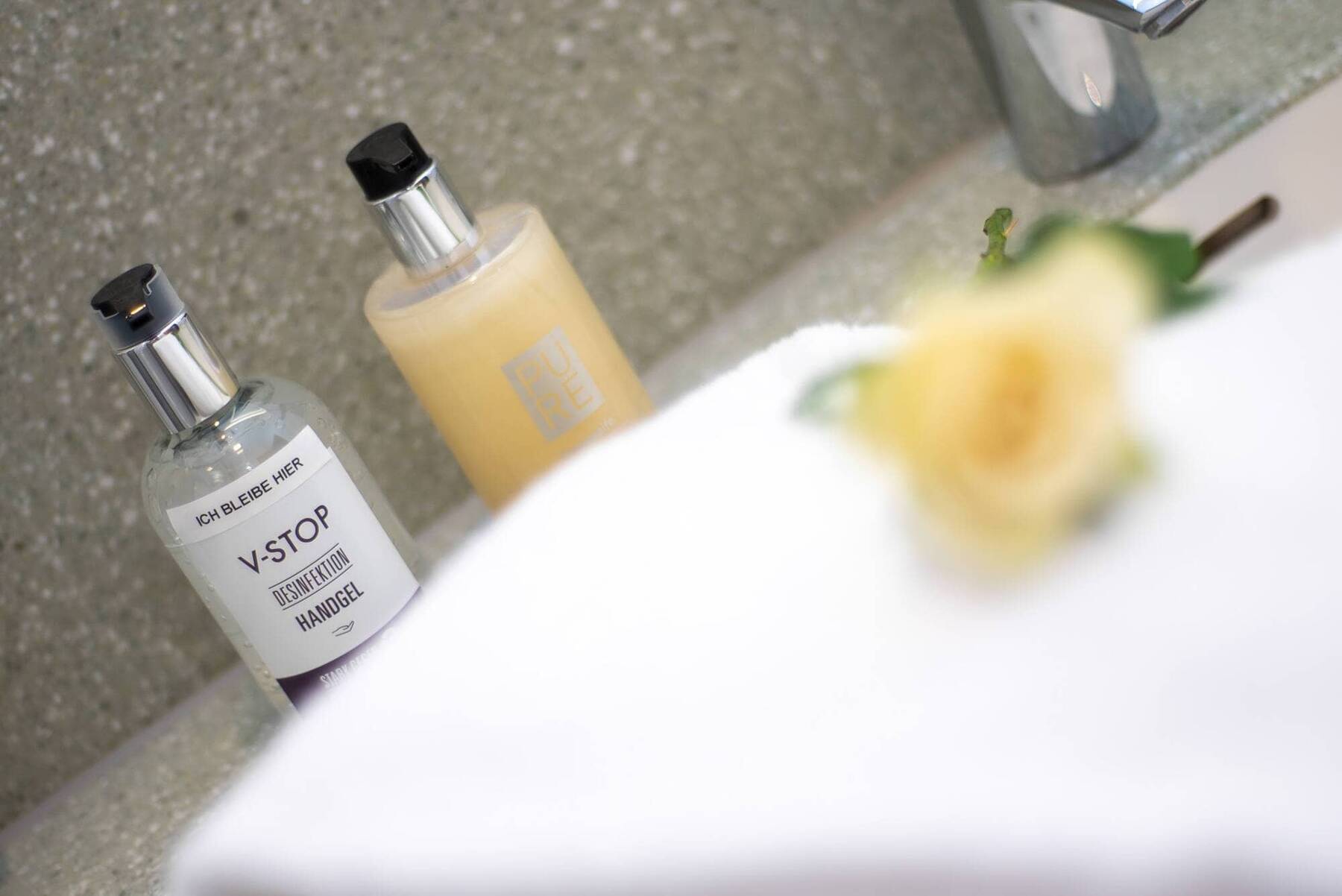 Handgel und Seife im Badezimmer vom Hotel Kastanienhof, im Vordergrund eine unscharfe gelbe Rose auf einem weißen Handtuch als farbiger Akzent.