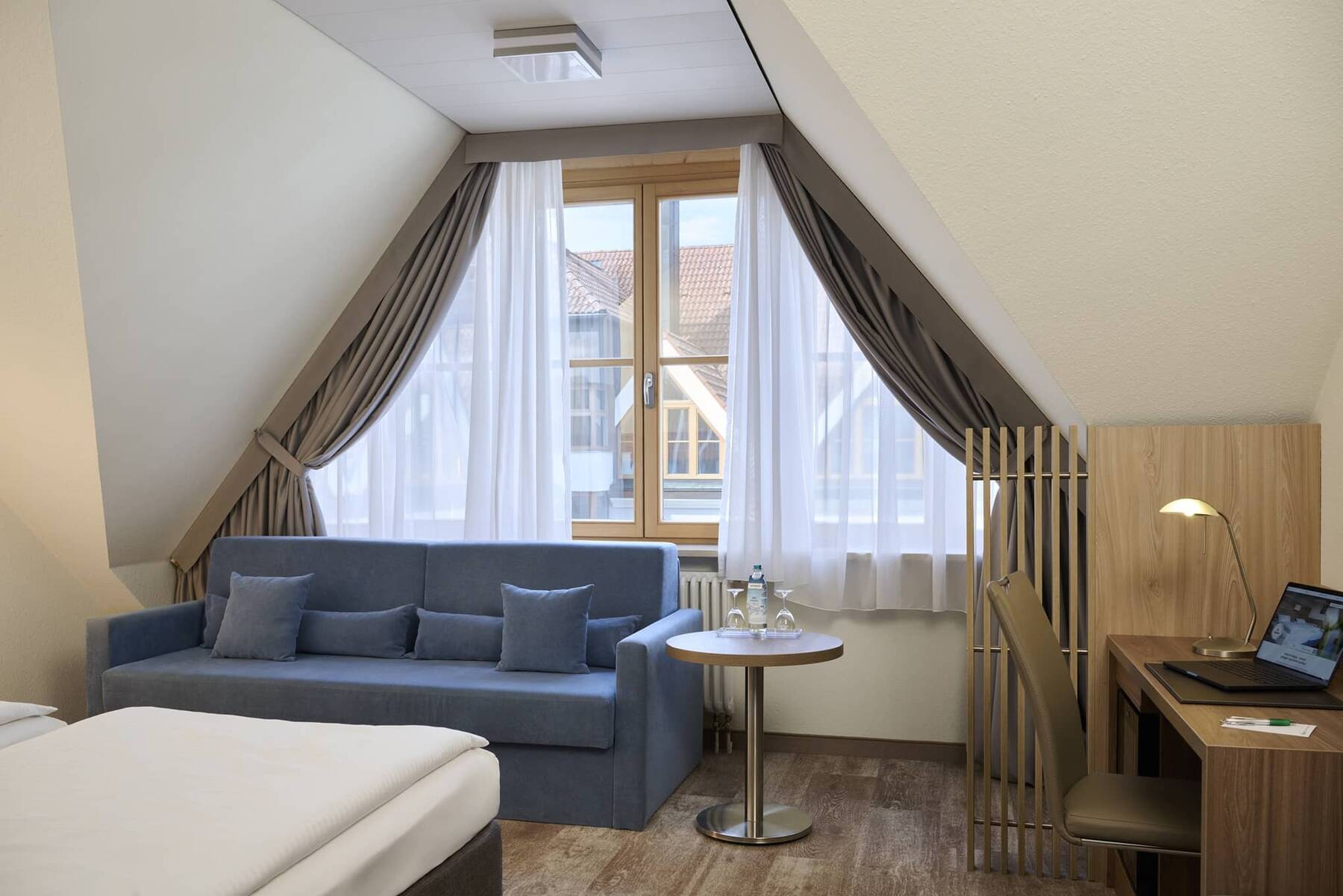 Helle Sitzecke im Doppelzimmer Superior im Hotel Kastanienhof Erding mit Sofa, Tisch, Arbeitsplatz und großem Fenster.