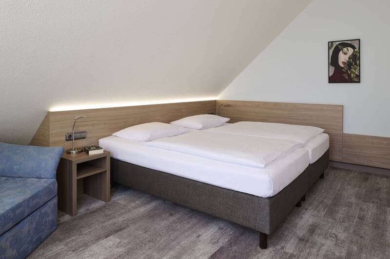 Heller Schlafbereich der Familiensuite im Hotel Kastanienhof Erding mit komfortablem Doppelbett, Dachschräge und gemütlicher Sitzecke.