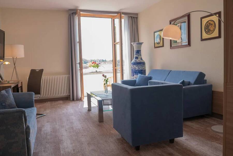 Eine Sitzlounge in einem der Hotel Kastaniehof Zimmer mit blauer Couch und blauem Sessel, dahinter eine geöffnete Terrassentür.