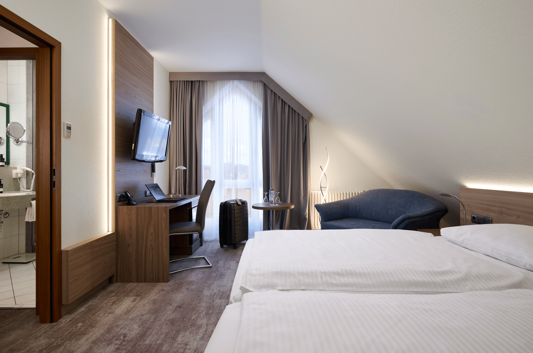 Spacious sleeping area of the Family Suite at Hotel Kastanienhof Erding with a comfortable double bed, sofa and workspace.