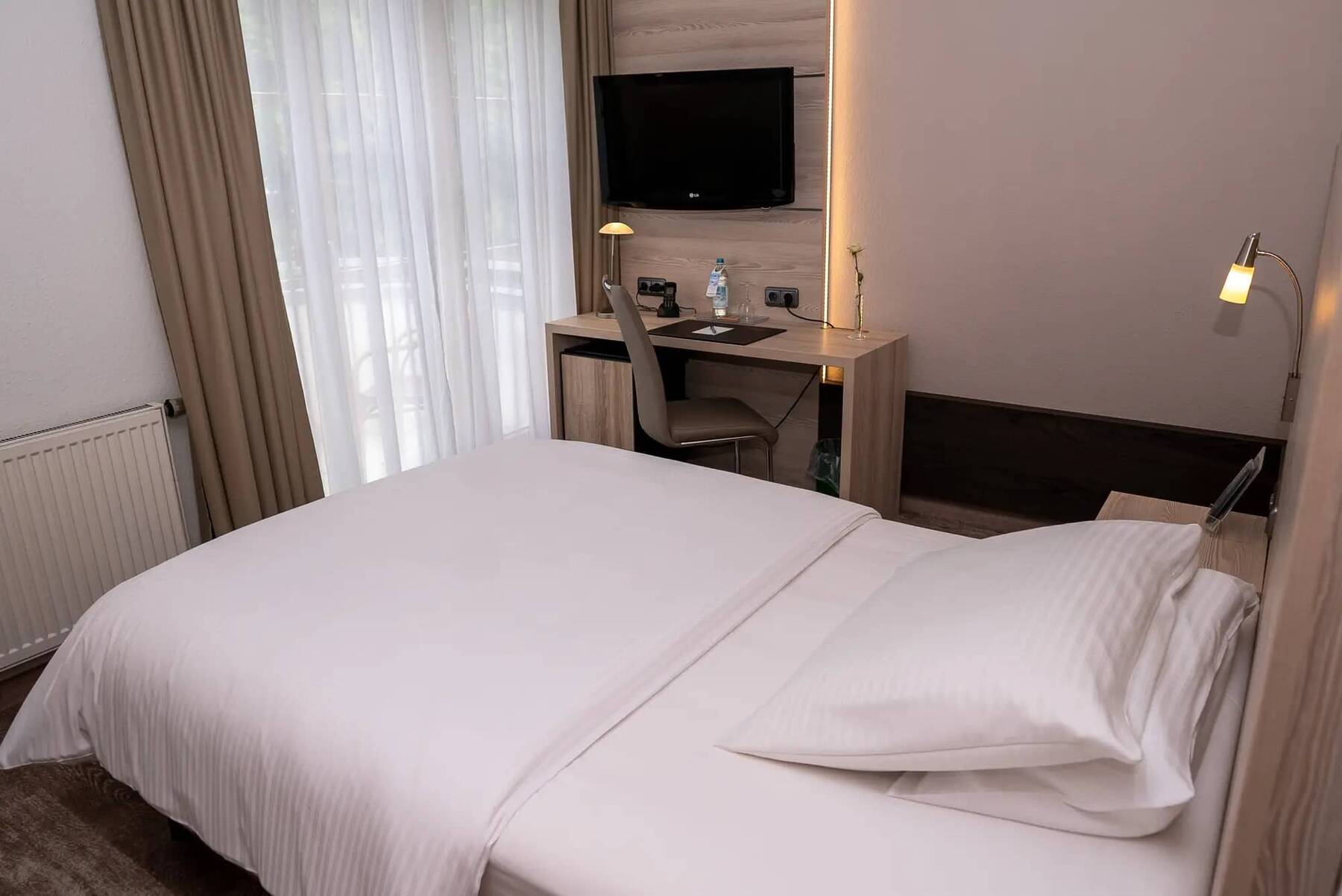 Einzelzimmer in der Familiensuite des Hotel Kastanienhof Erding mit Schreibtisch, Flachbild-TV, breitem Bett und Zugang zum Balkon.