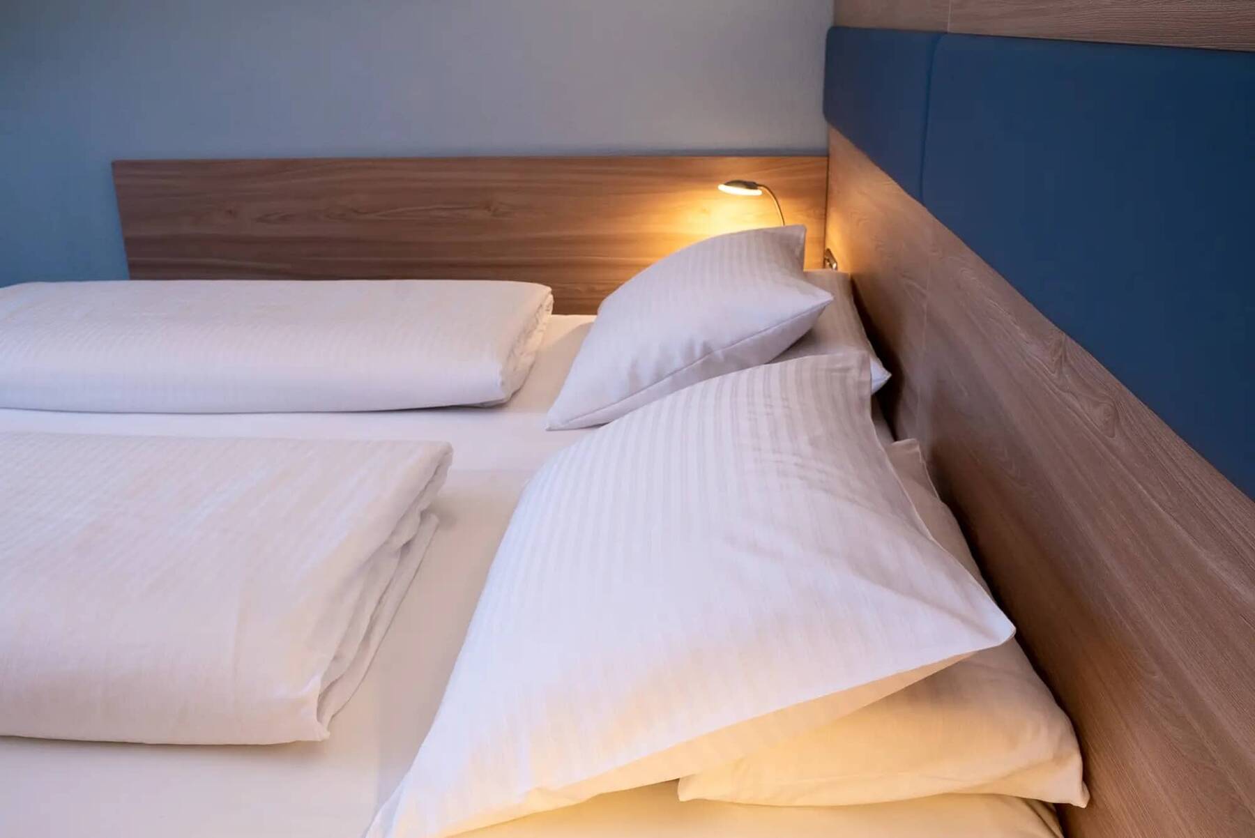 Modern eingerichtetes Doppelzimmer im Hotel Kastanienhof Erding mit hellem Holzdesign, bequemen weißen Kopfkissen und Bettdecken, Leselampe am Bettkopf.