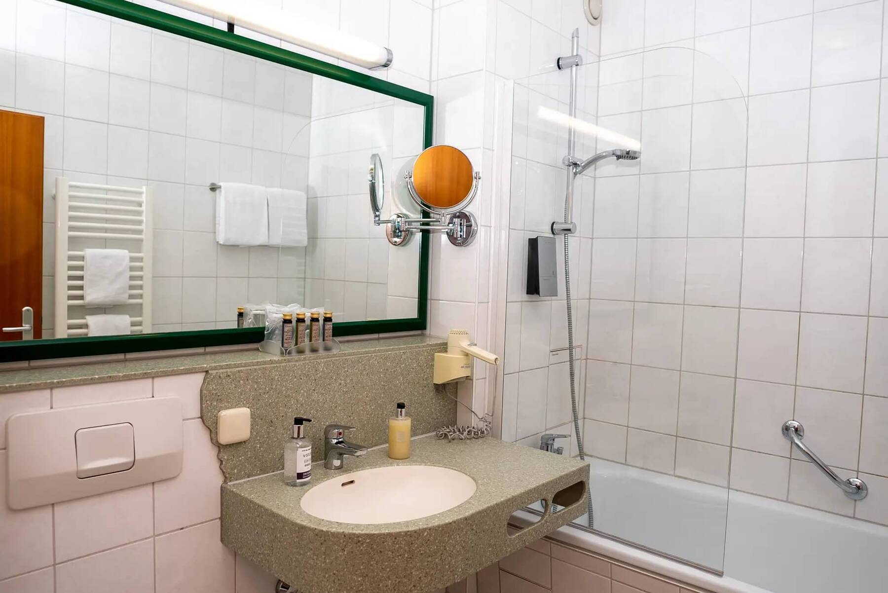 Badezimmer der Familiensuite im Hotel Kastanienhof Erding mit Badewanne, Duschkombination, großem Spiegel und Pflegeprodukten für die ganze Familie.
