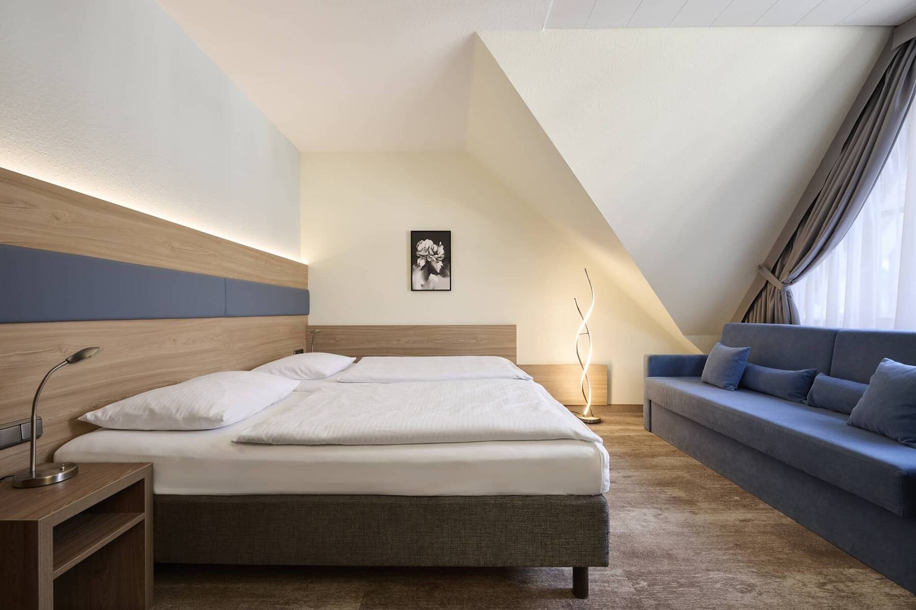 Geräumiges Doppelzimmer Superior im Hotel Kastanienhof Erding mit komfortablem Doppelbett, Sofa und gemütlicher Dachschräge.