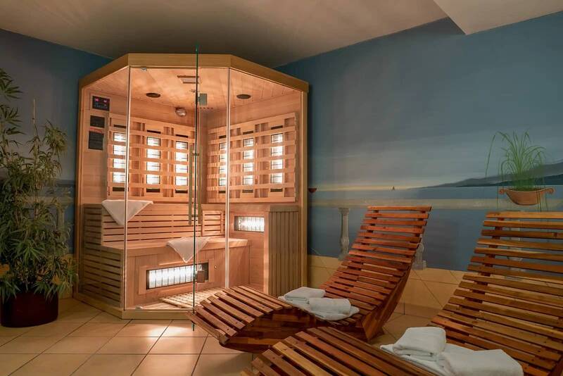 Wellness area in the Hotel Kastanienhof Erding with modern infrared cabin, wooden deckchairs and a relaxed atmosphere in front of a mural with a lake motif.