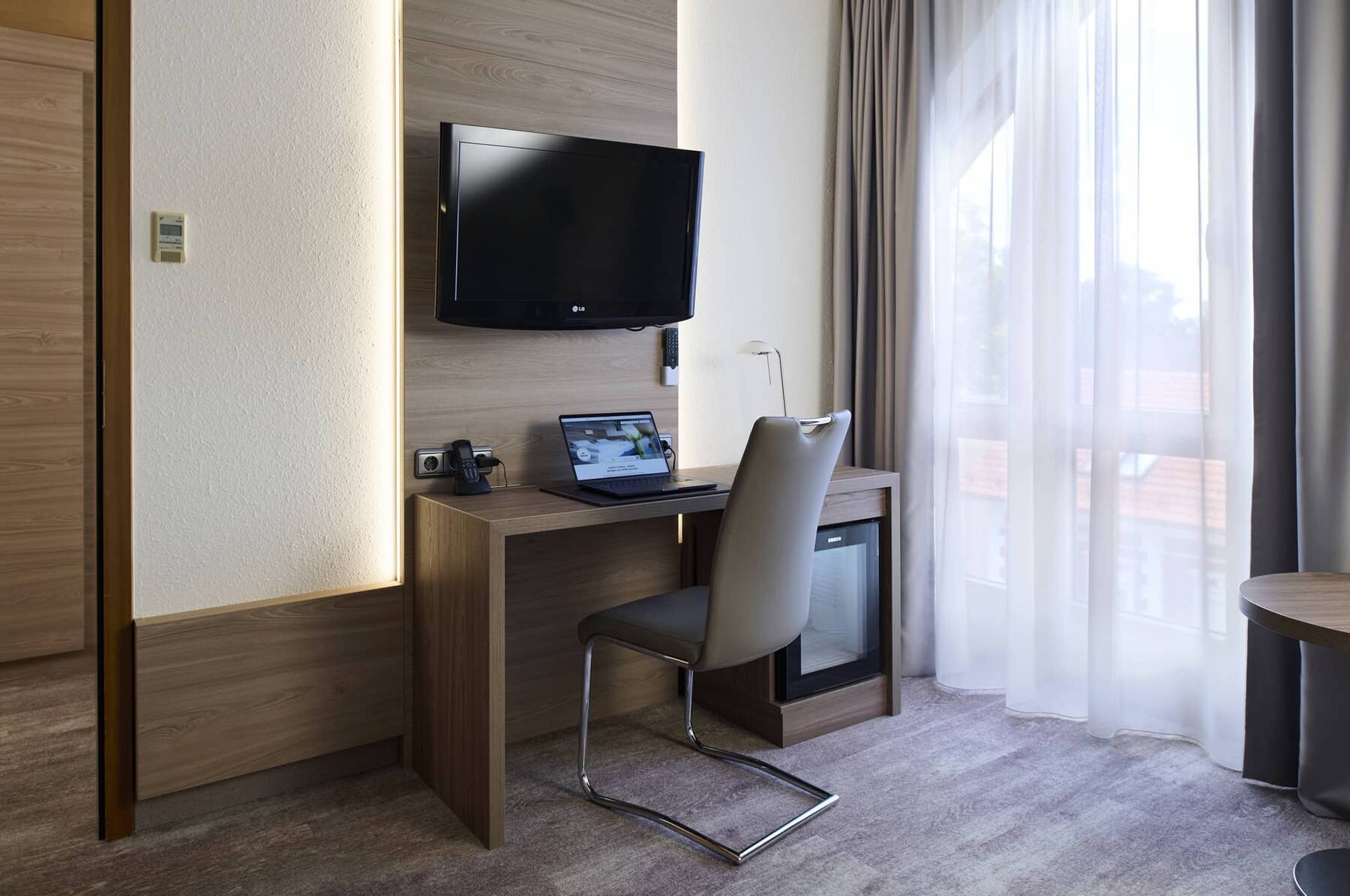 Praktischer Arbeitsbereich der Familiensuite im Hotel Kastanienhof Erding mit Schreibtisch, TV und großem Fenster.